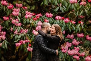 Couple embracing among blooming pink rhododendron flowers in garden setting.