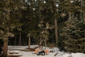 Two people sitting on bench in snowy forest landscape.
