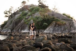 A couple embraces on rocky coastal terrain with a dramatic cliff backdrop at sunset.