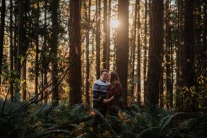 Sunlit forest engagement photo with golden light streaming through tall trees.