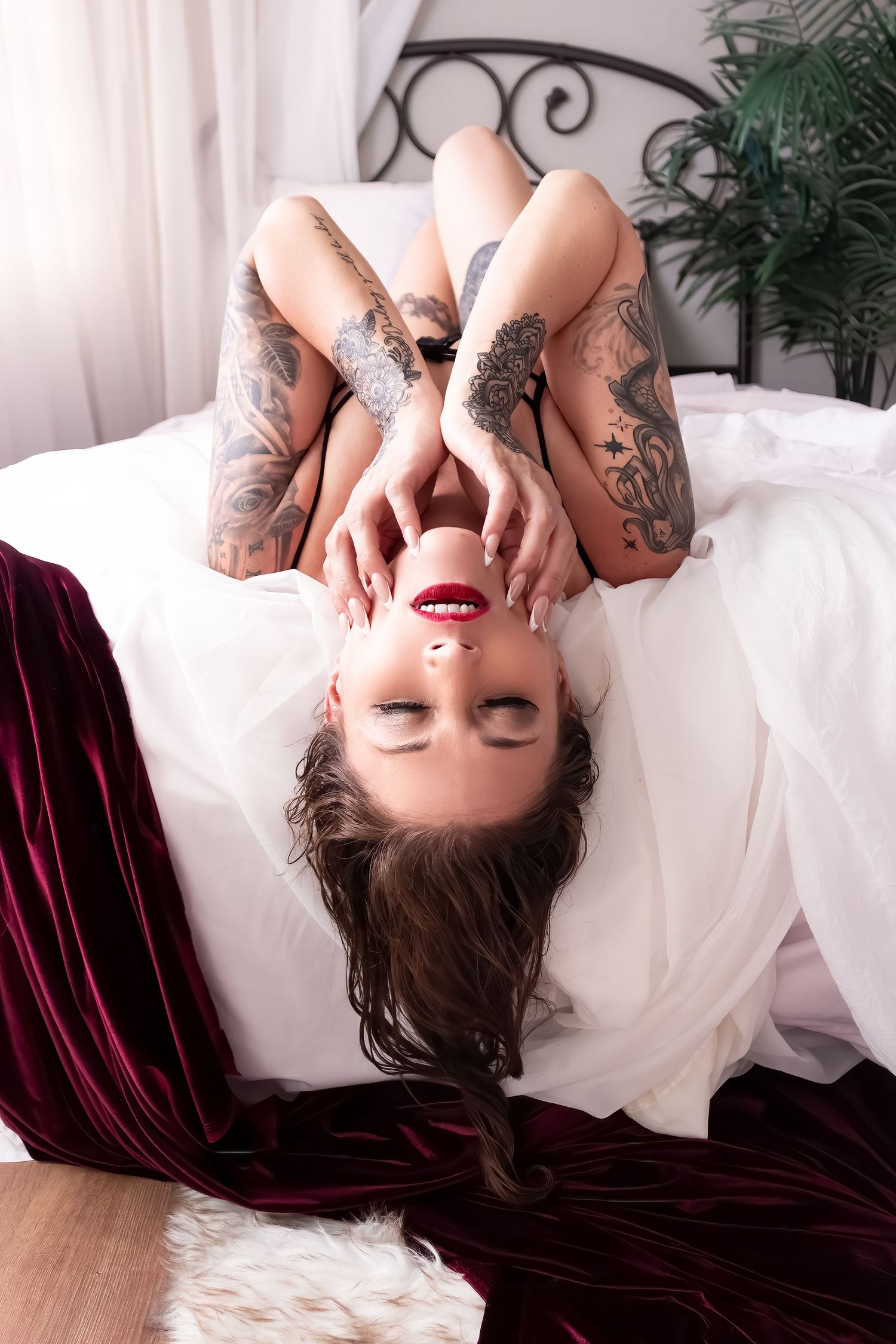 Boudoir Photography in Colorado Springs, Hot tattooed woman with red lipstick lying on bed with her head hanging off
