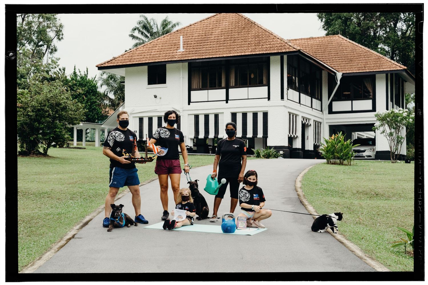 A family stands outside their home during the pandemic, wearing masks