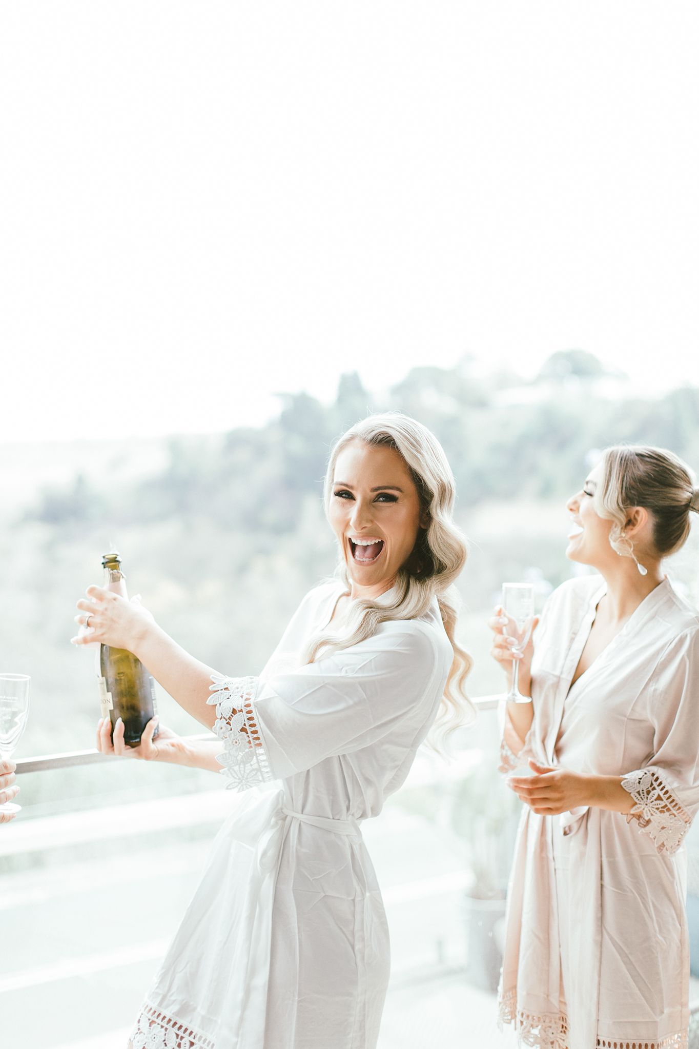 People in white robes celebrating with champagne by a bright window.