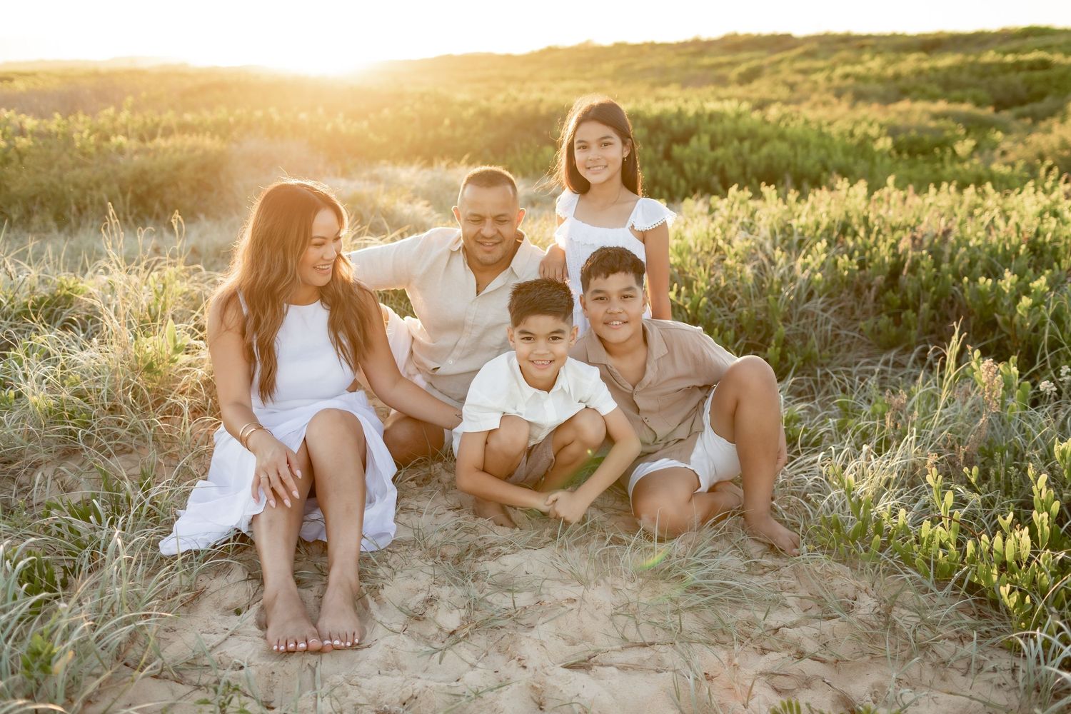 Family sitting together on sand dunes during golden hour sunset photoshoot.