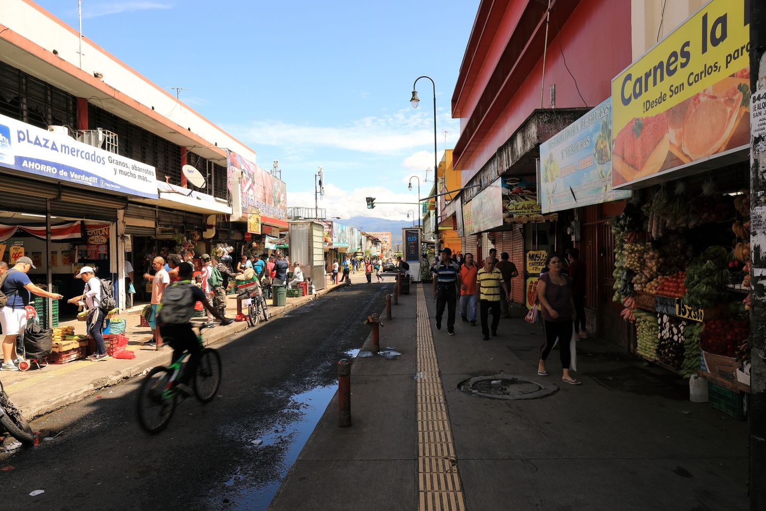 Busy street market with shops and pedestrians in Latin American urban setting.
