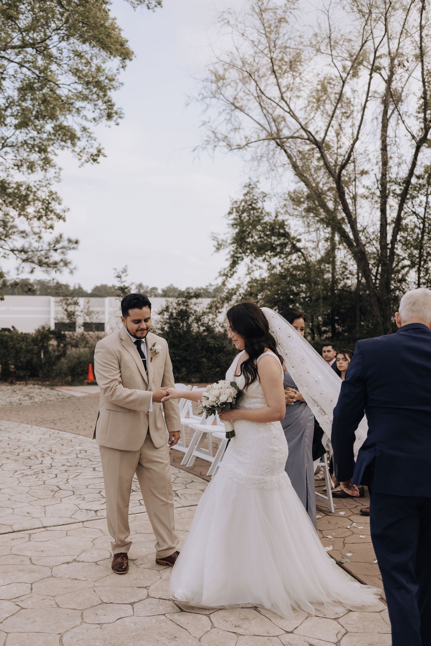 A formal wedding ceremony takes place on a stone patio surrounded by trees and natural scenery.