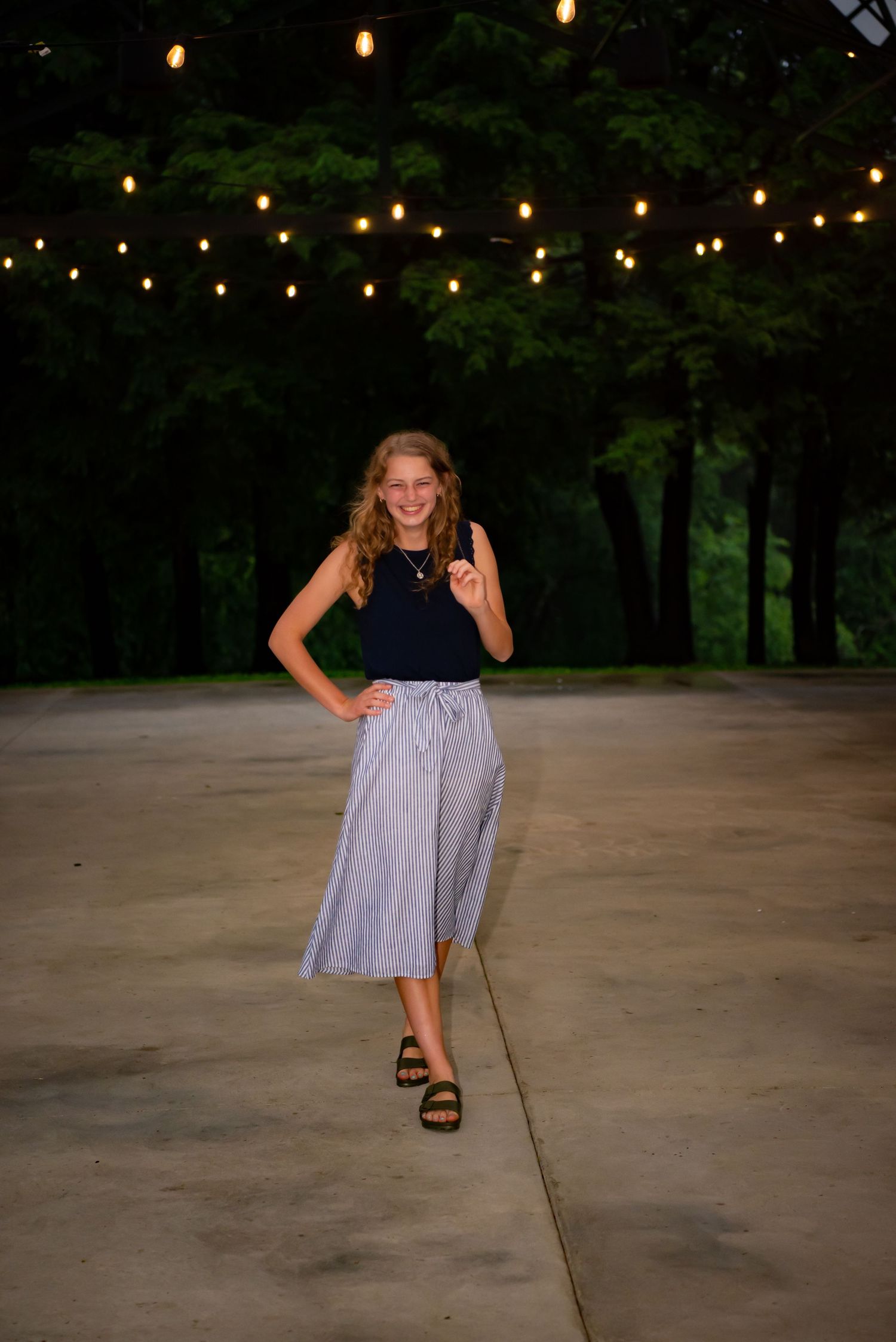 high school senior girl with hand on hip dancing with party lights above