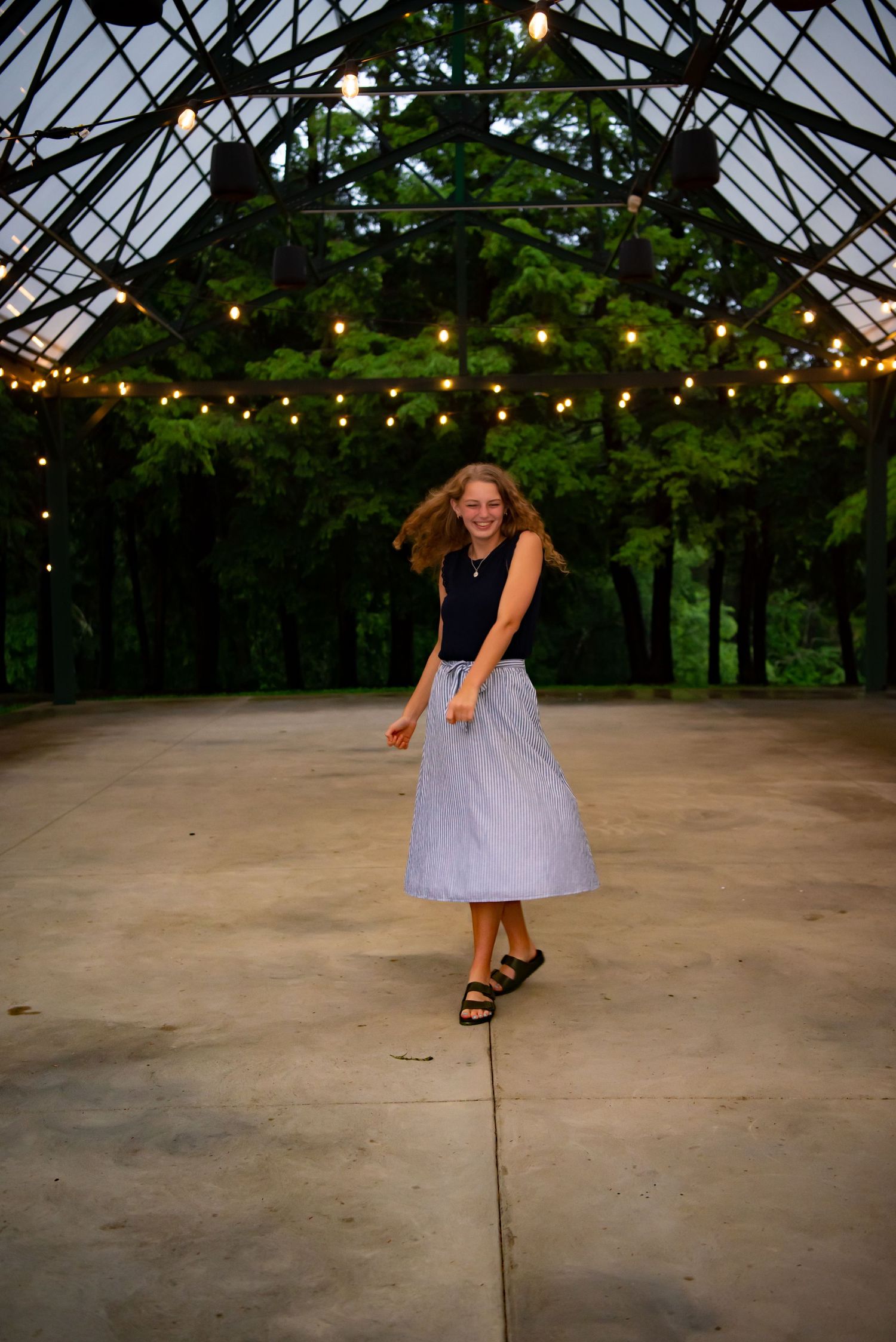 high school senior girl under a clear roof dancing at hartwood acres with lights