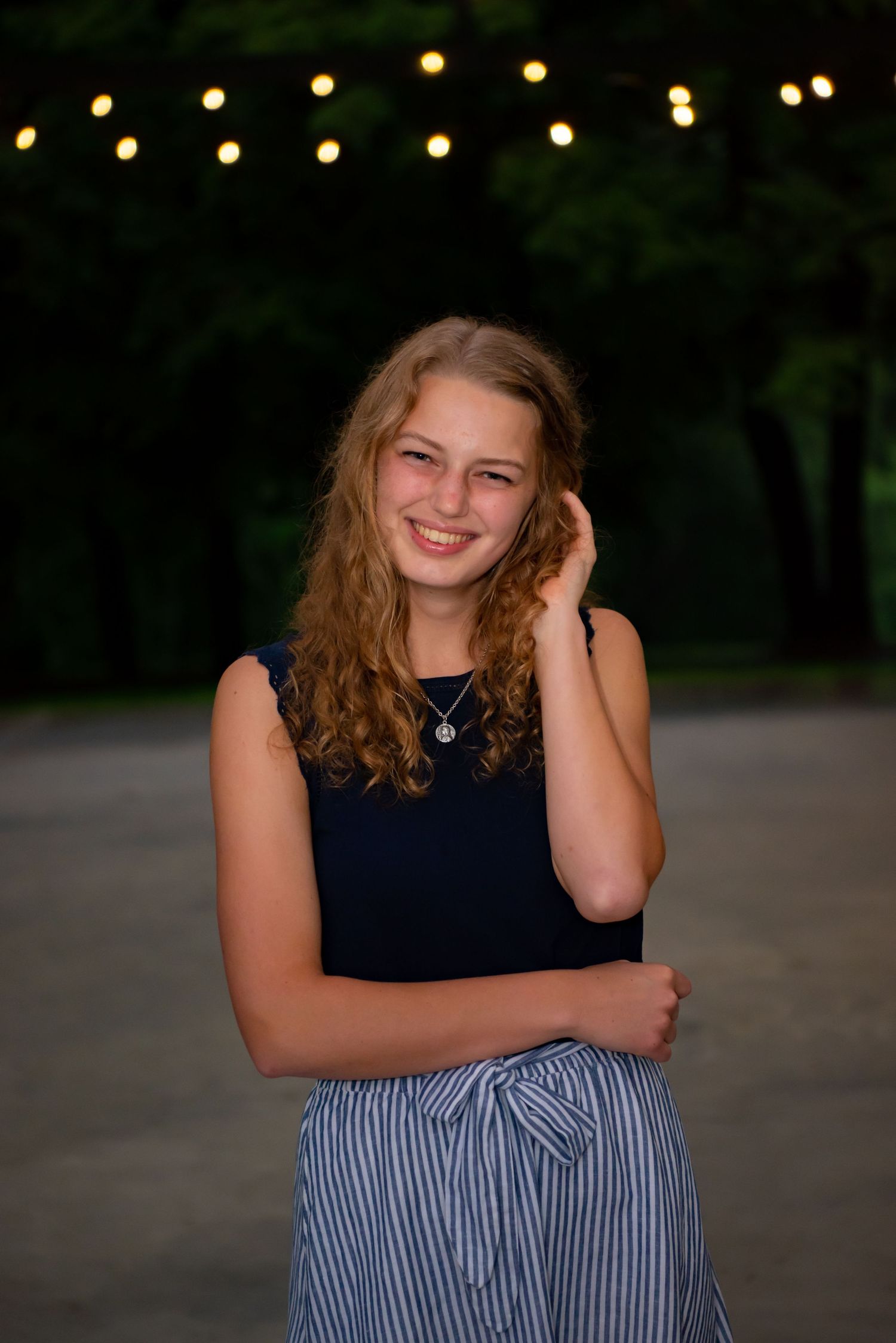 high school senior girl playing with hair while posing for portrait with green trees in background