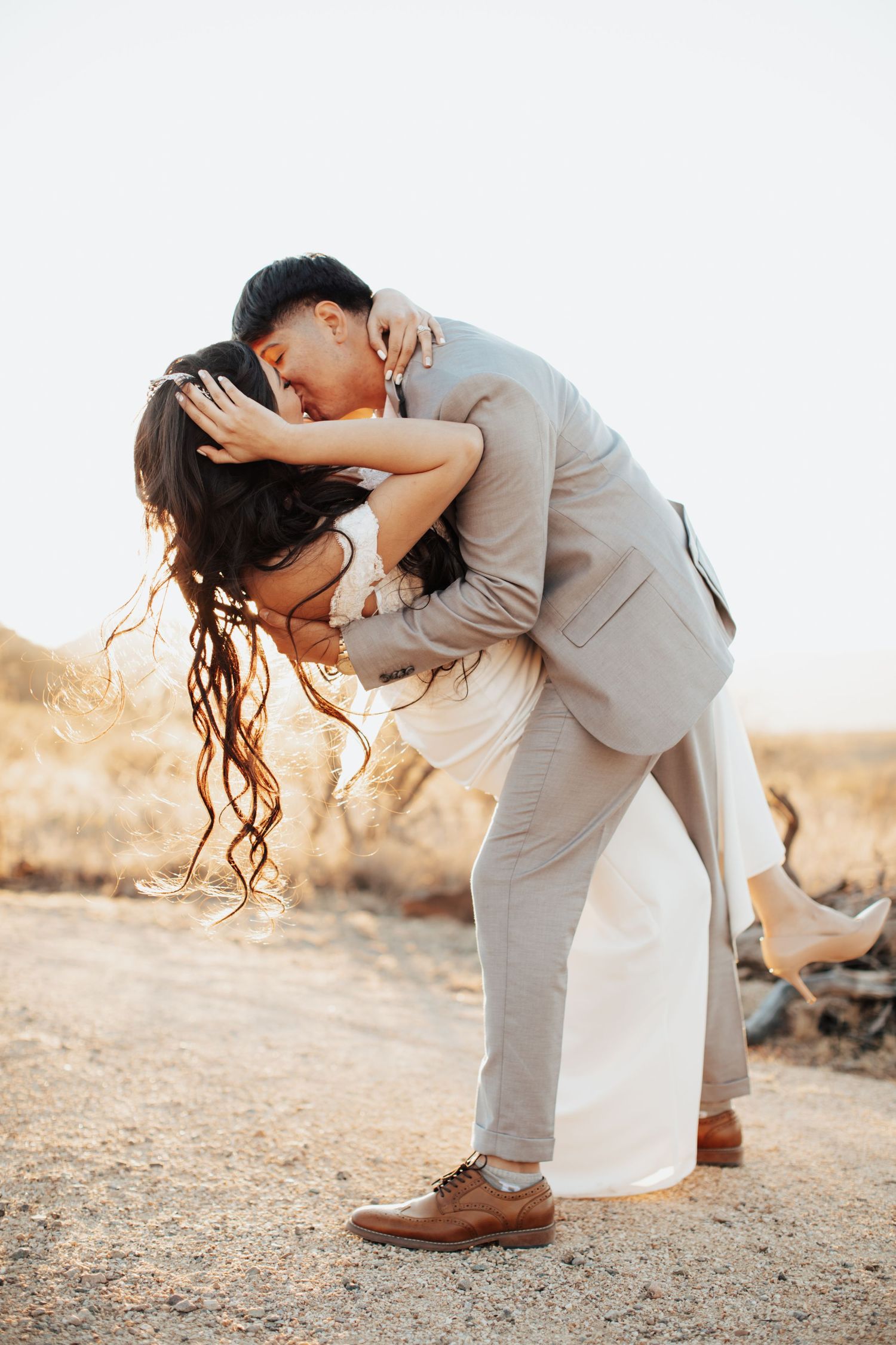 Tucson couples photo of a man lifting and kissing his partner in a desert setting with light sand and warm tones.