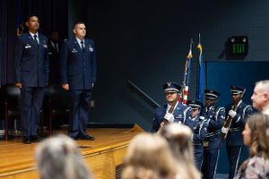 A military honor guard ceremony with service members and audience members in an auditorium.