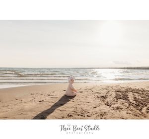 Serene beach scene with figure sitting on sand during sunset.