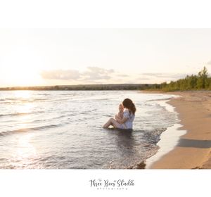 People sitting in shallow water at the beach during sunset with waves gently rolling in.