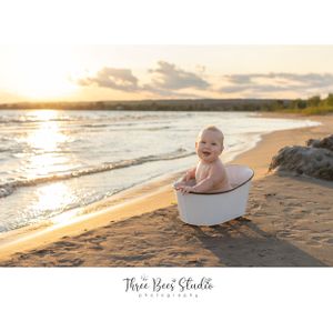 Baby sitting in white basin on sandy beach during golden sunset.