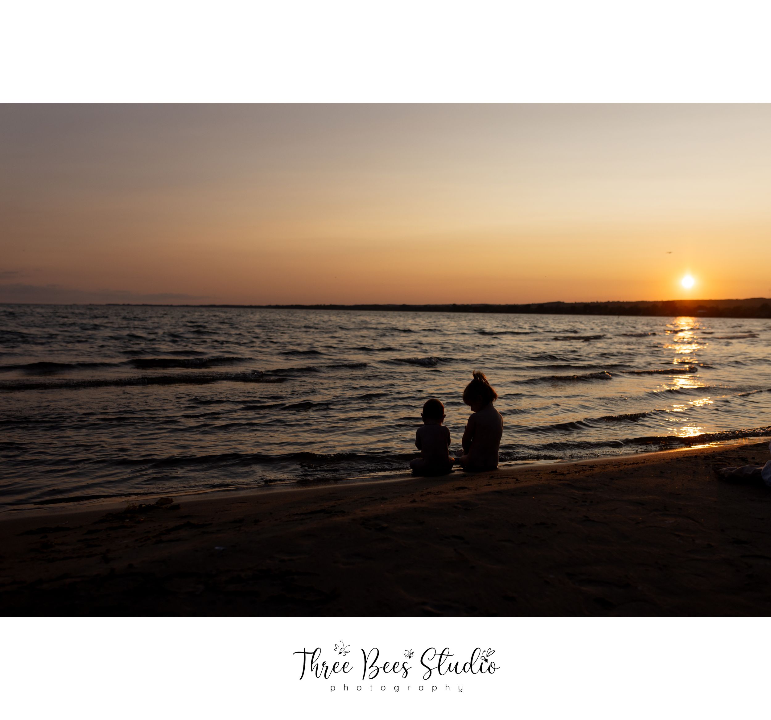 Silhouettes of people sitting on beach watching sunset over lake or ocean.