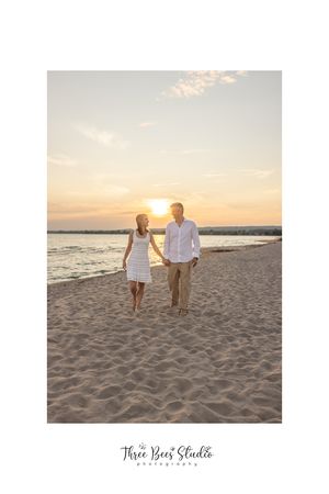 Couple walking hand in hand on sandy beach during golden sunset.