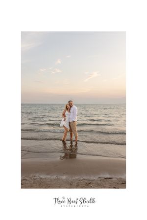 Couple embracing on beach at sunset with waves rolling in behind them.