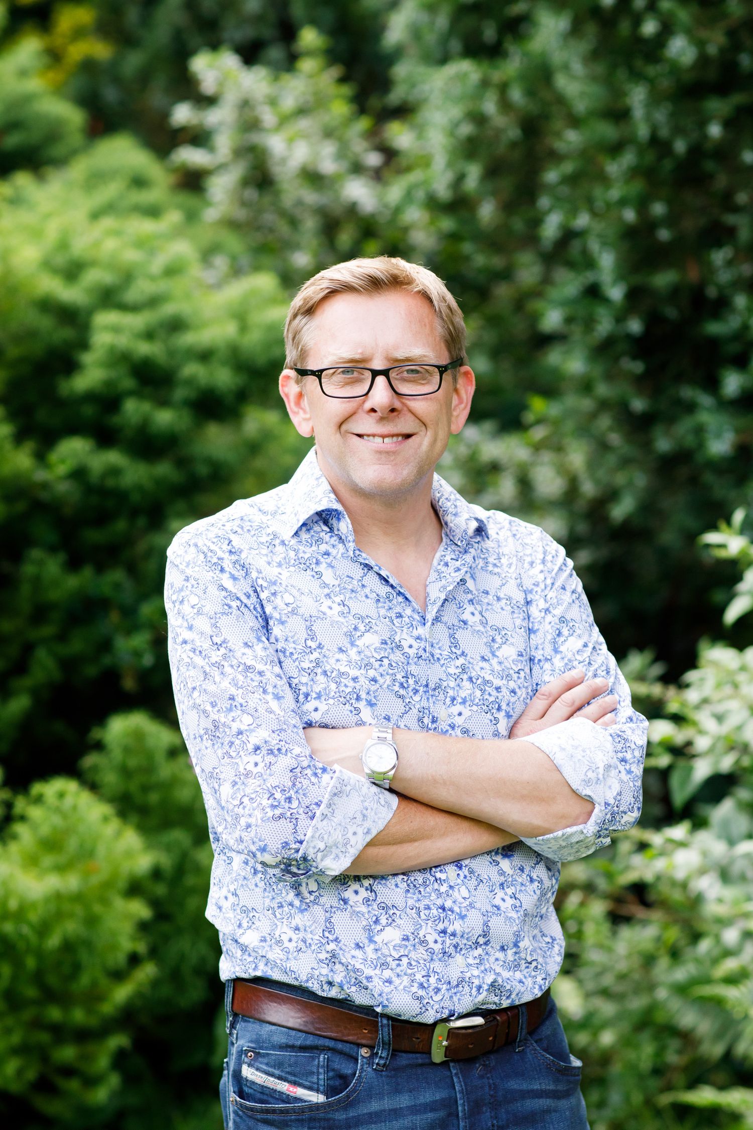 Casual outdoor portrait of person in floral shirt and glasses against green foliage during business branding photoshoot.