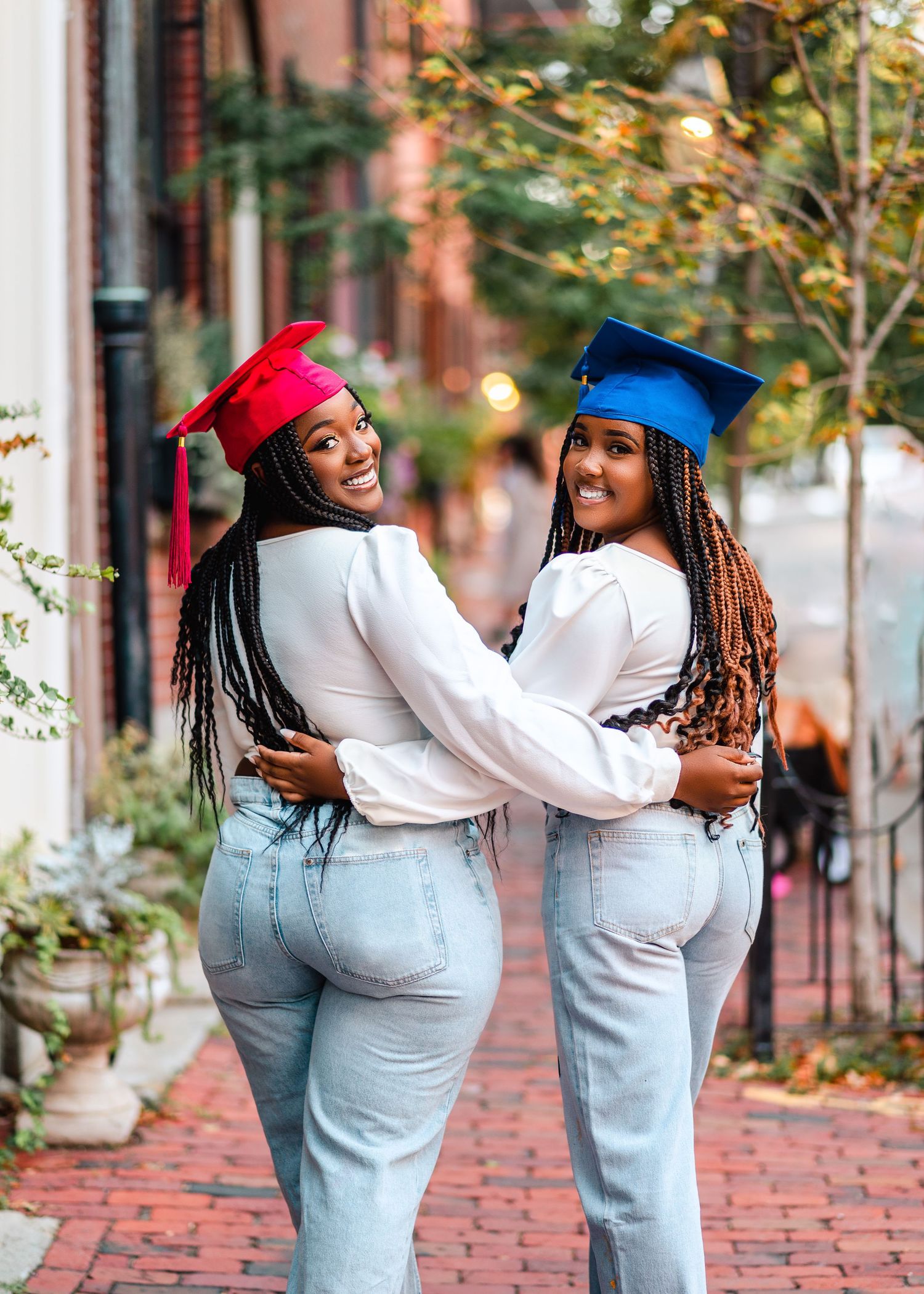 Graduation celebration photo with two graduates in blue and red caps on brick sidewalk.