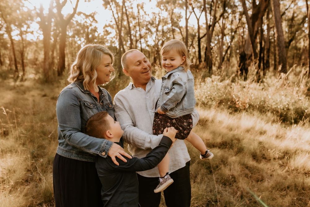 Playful family photoshoot in a sunlit field with warm sepia tones.