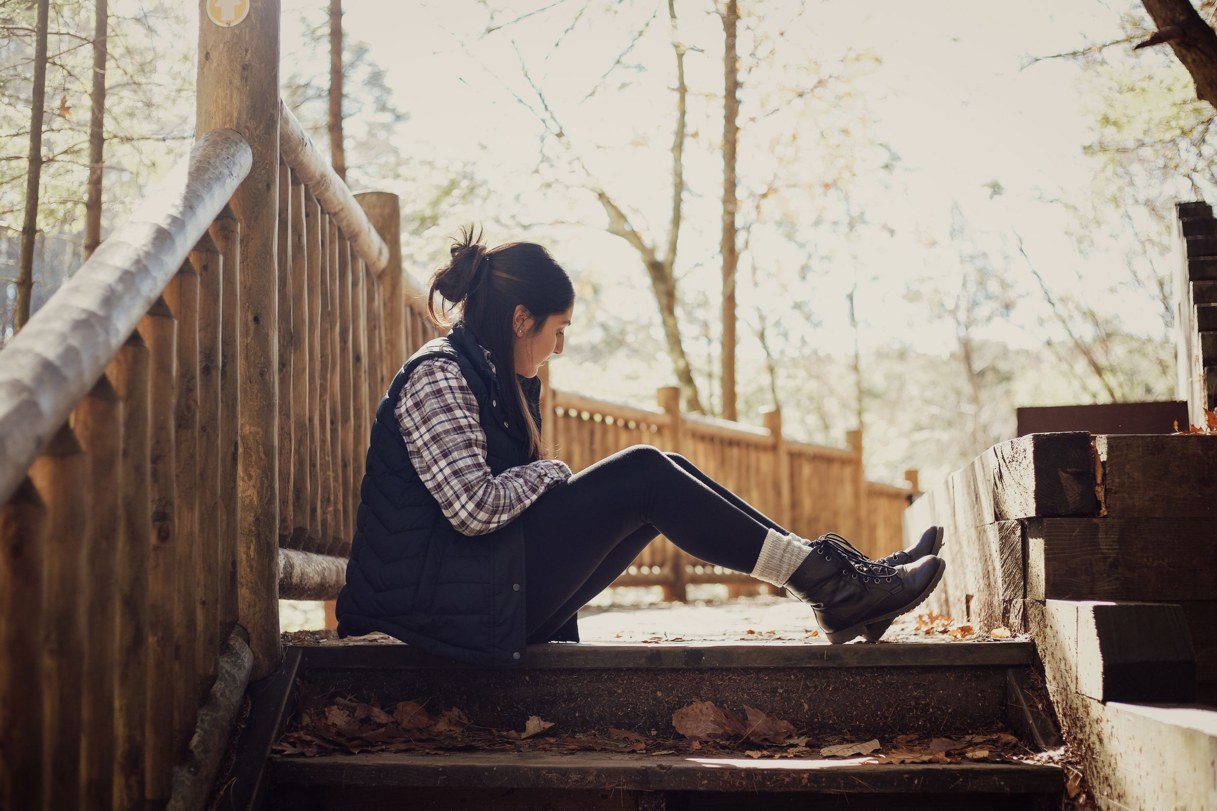 A person in casual attire sits on wooden stairs in a forest setting.