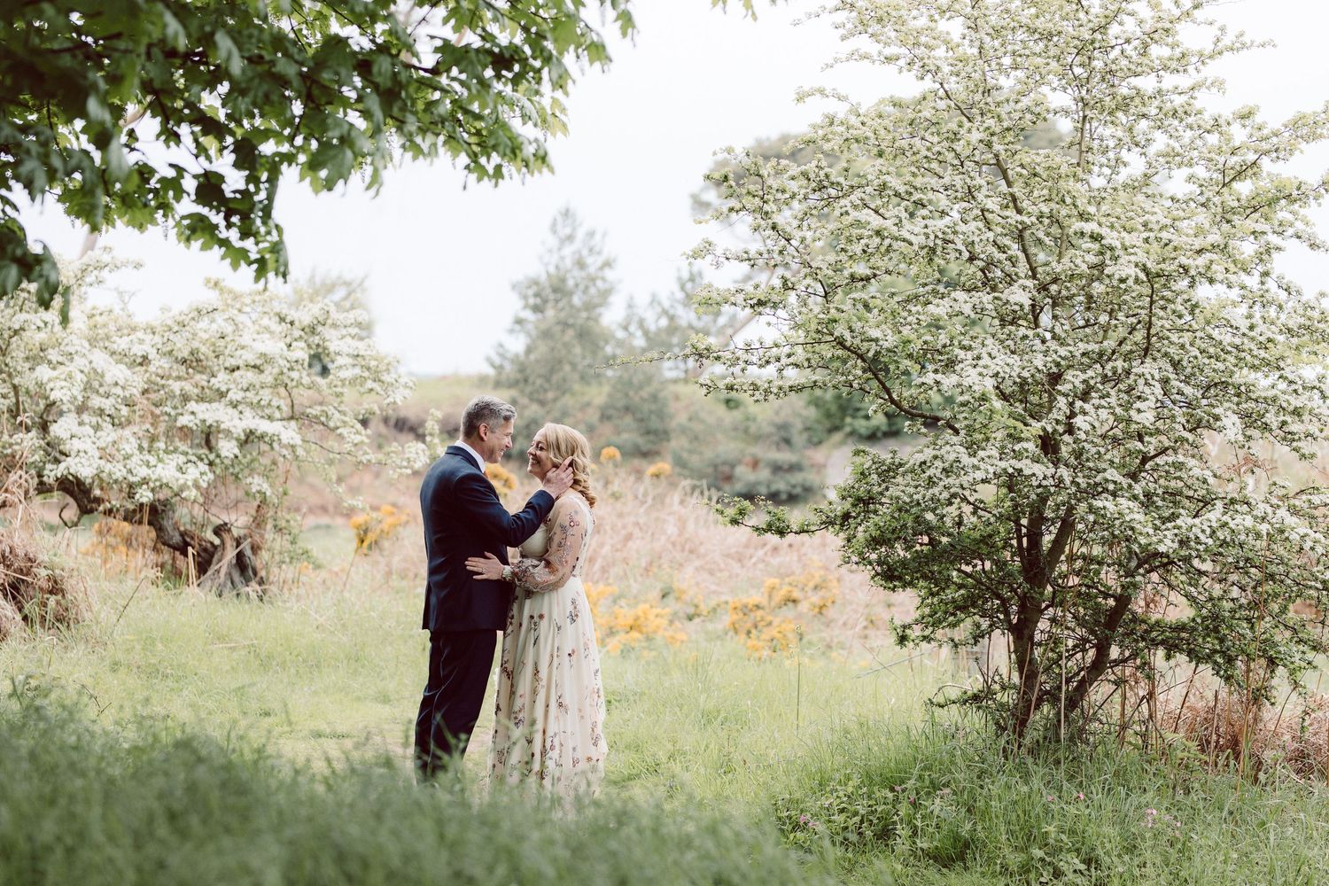 Wedding couple walking through a natural path surrounded by blooming spring trees.