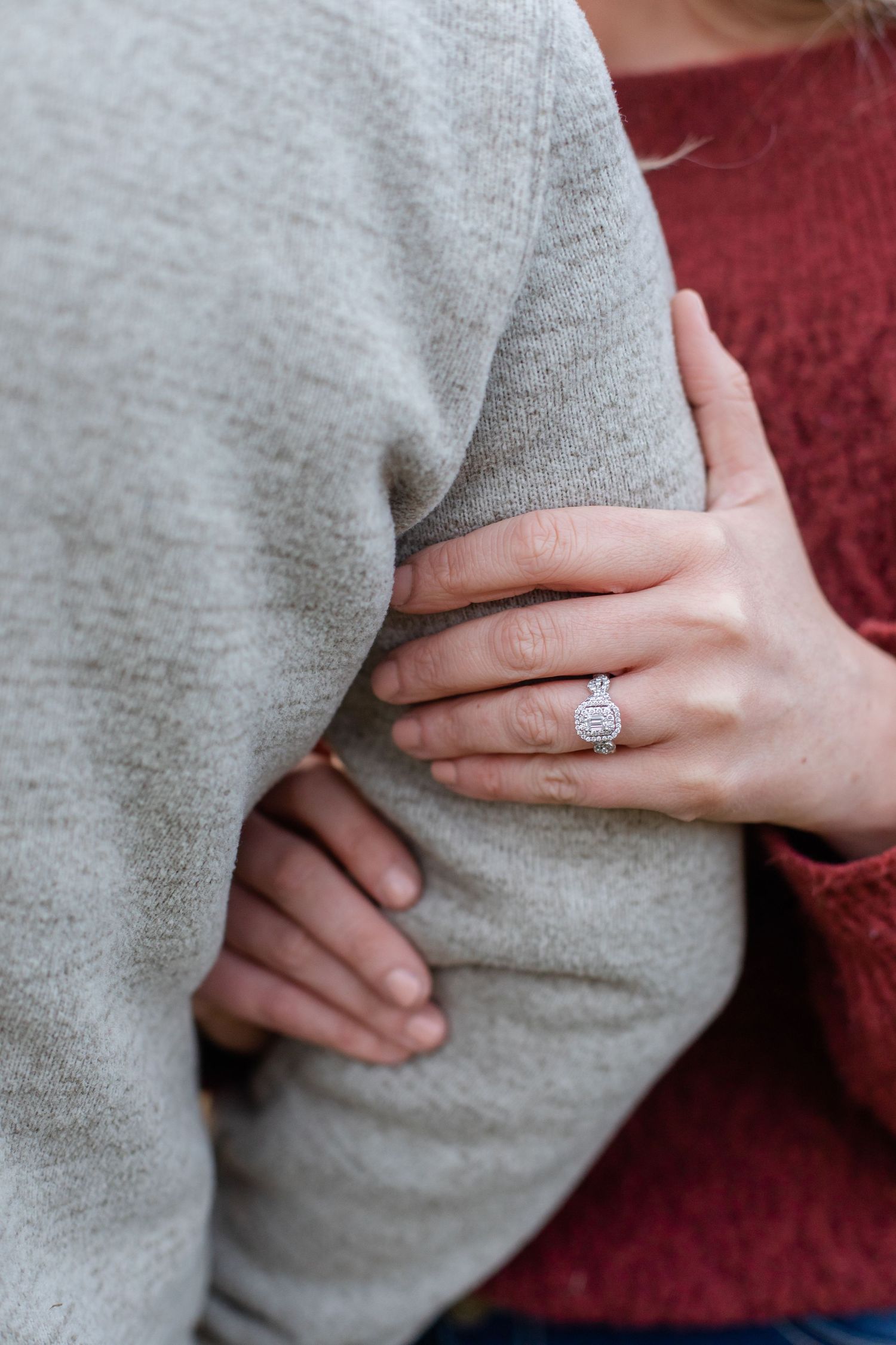 Close-up of hands showing off an engagement ring against a grey sweater.