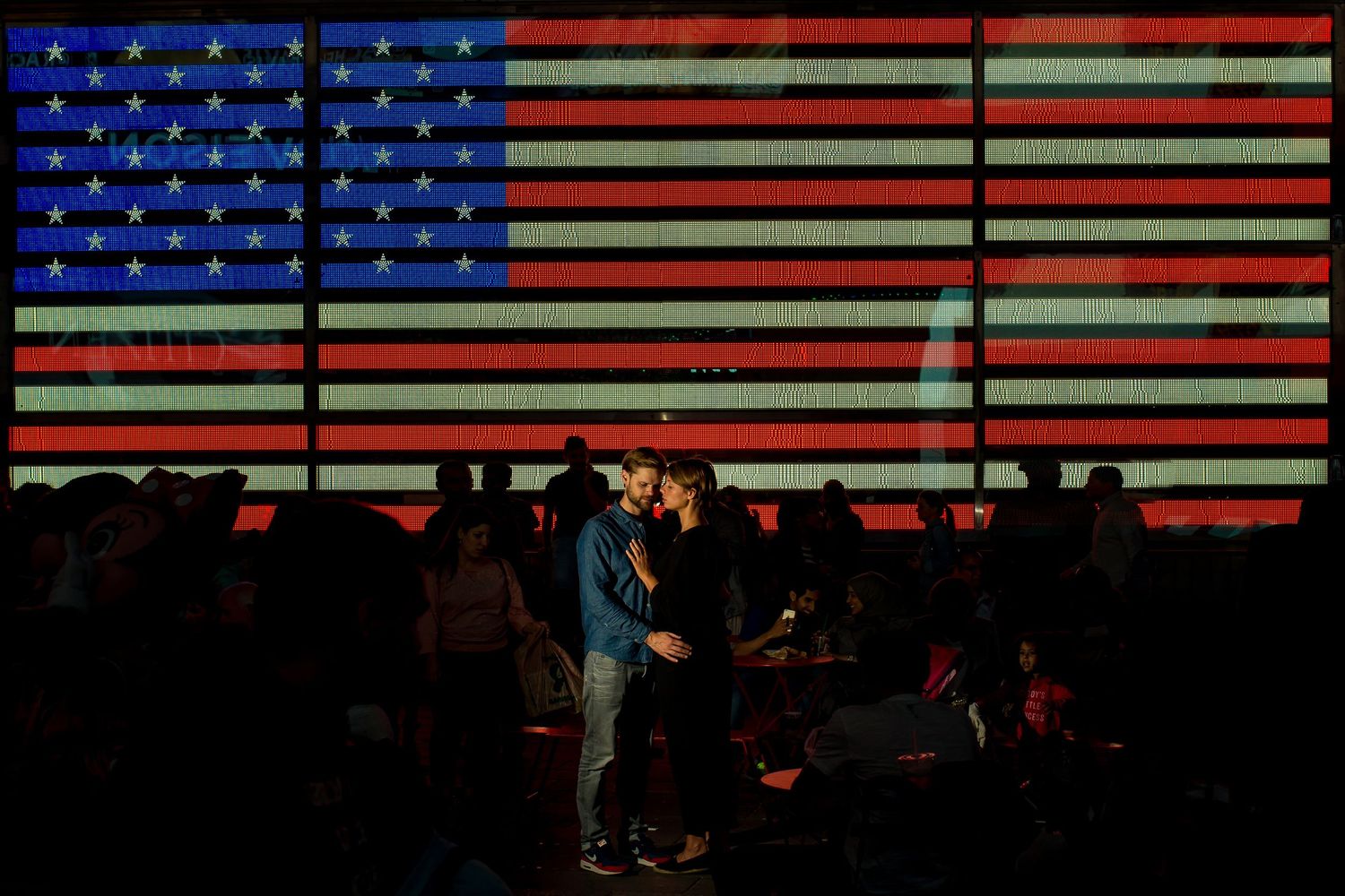 A silhouetted couple stands against a glowing American flag backdrop during an evening performance.