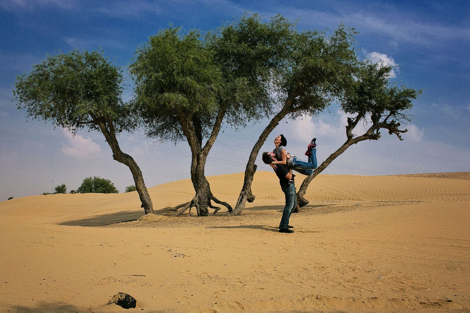 People strike acrobatic poses among trees in a desert landscape under blue skies.