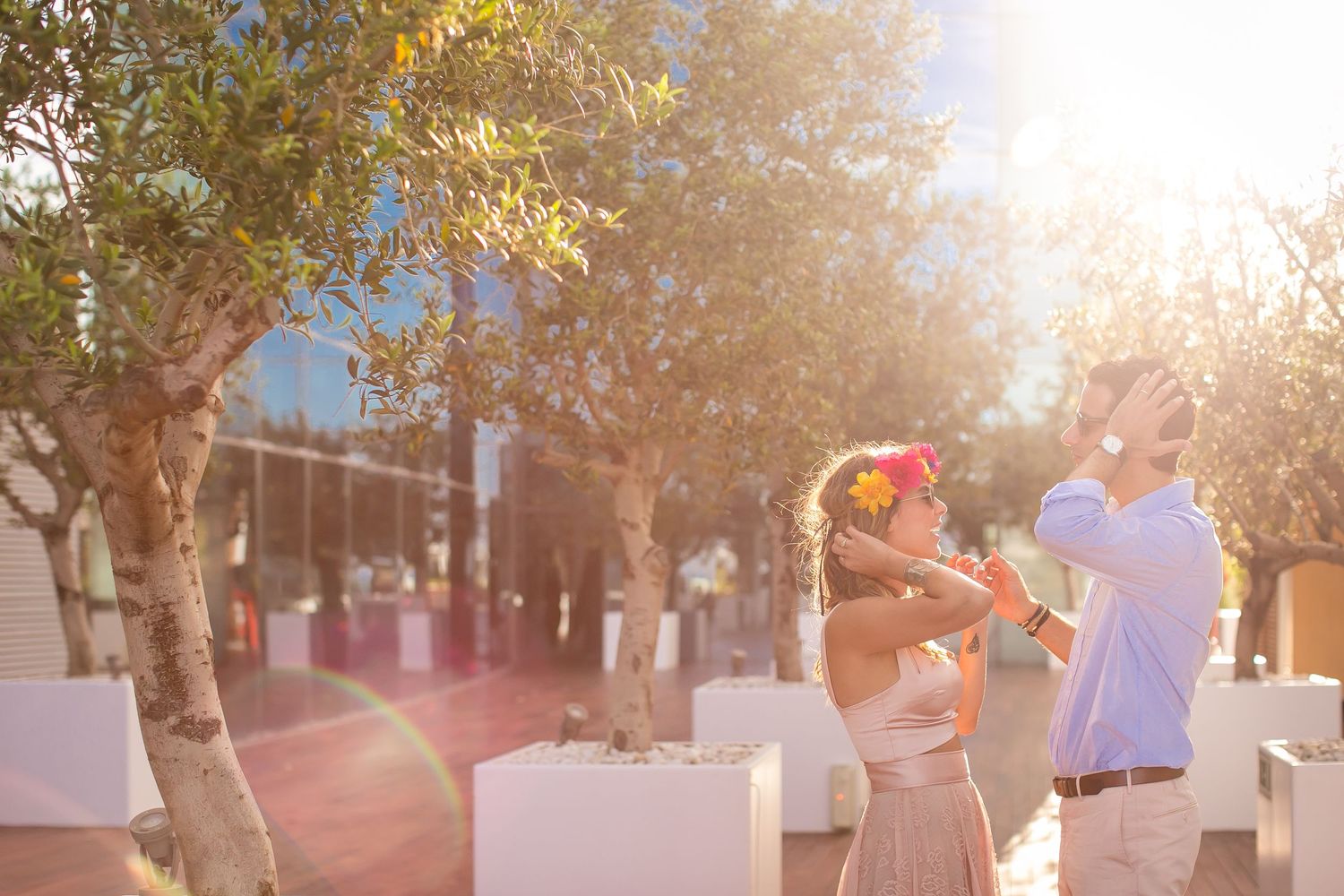 Couple dancing together in sunlit outdoor setting with trees and white decor.