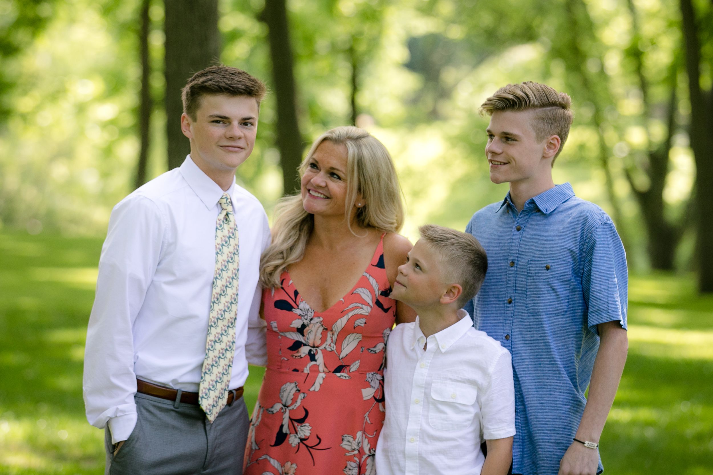 A family of four poses together on a sunny day in a green park setting.
