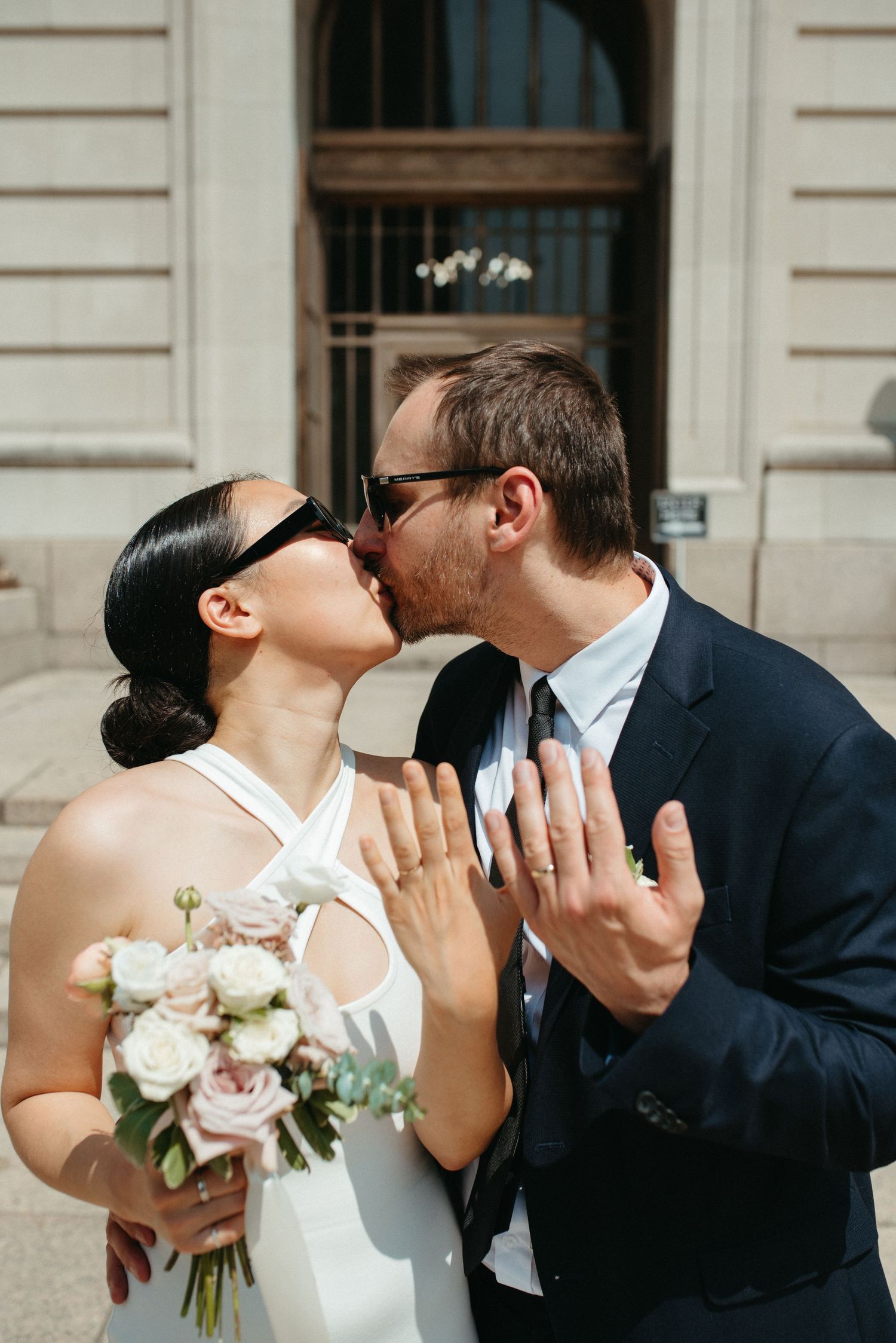 Couple shares romantic moment with white bouquet outside historic building entrance.