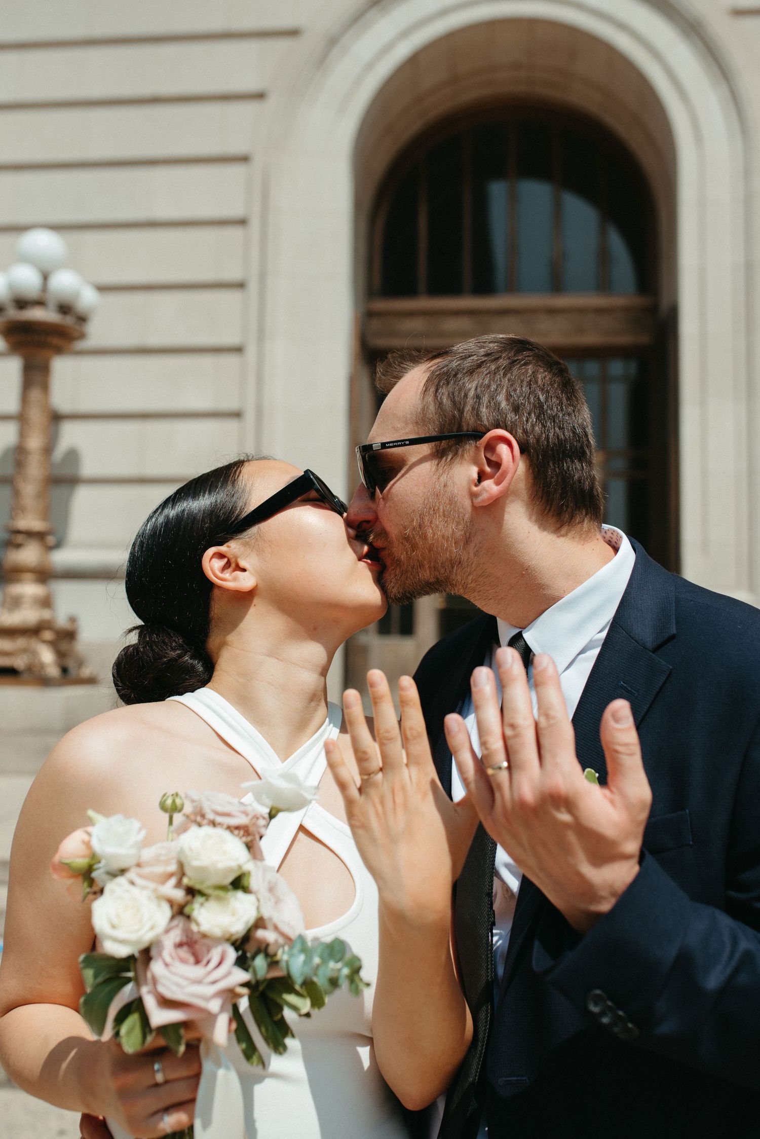 Couple shares celebratory moment with white bouquet on courthouse steps.
