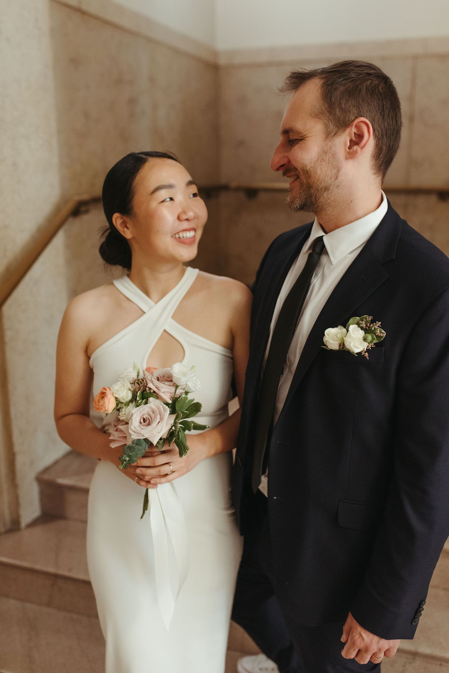 A candid moment of a happy couple sharing laughter on their wedding day in a classic building.