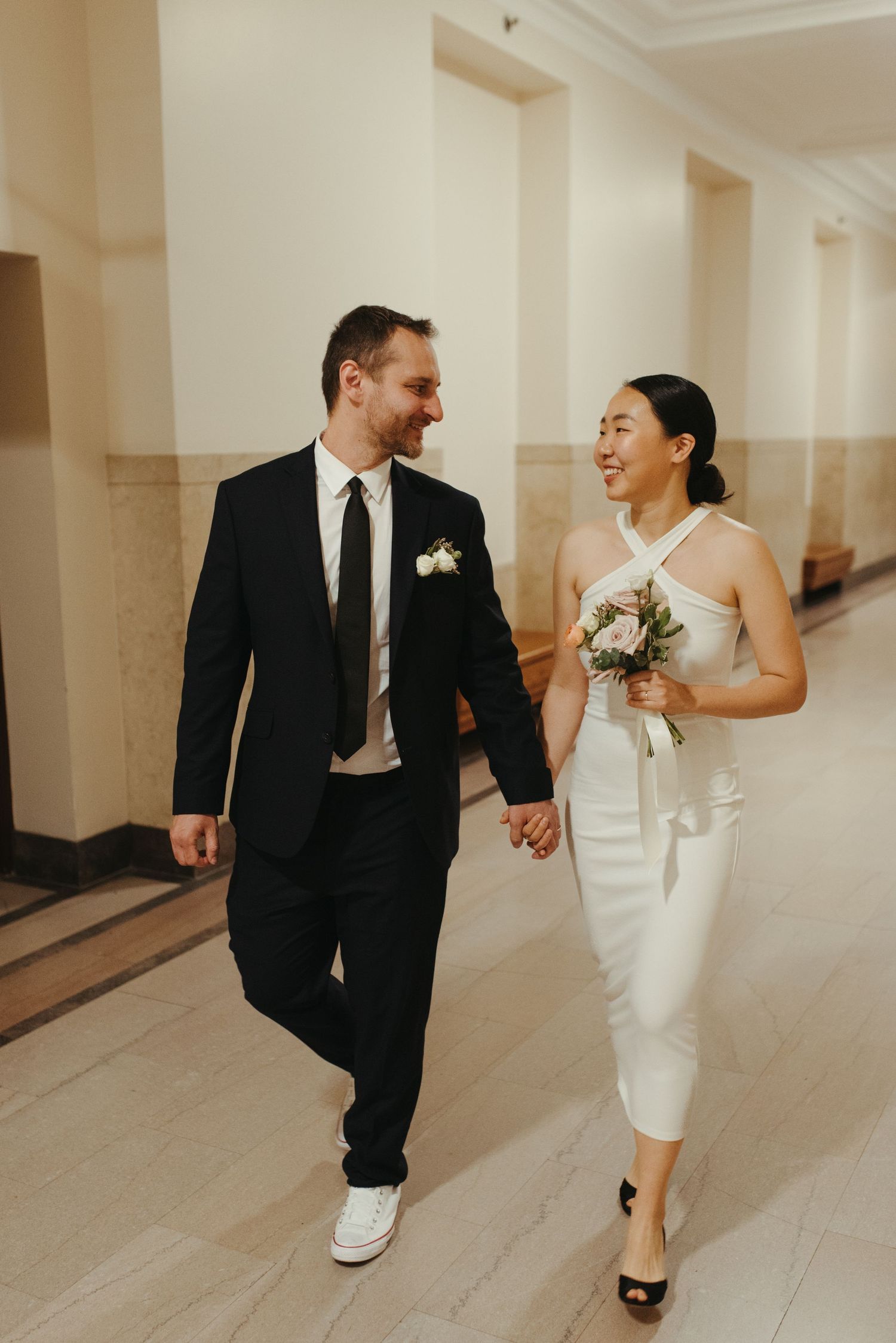 A joyful couple walks hand in hand down a hallway during their wedding celebration.