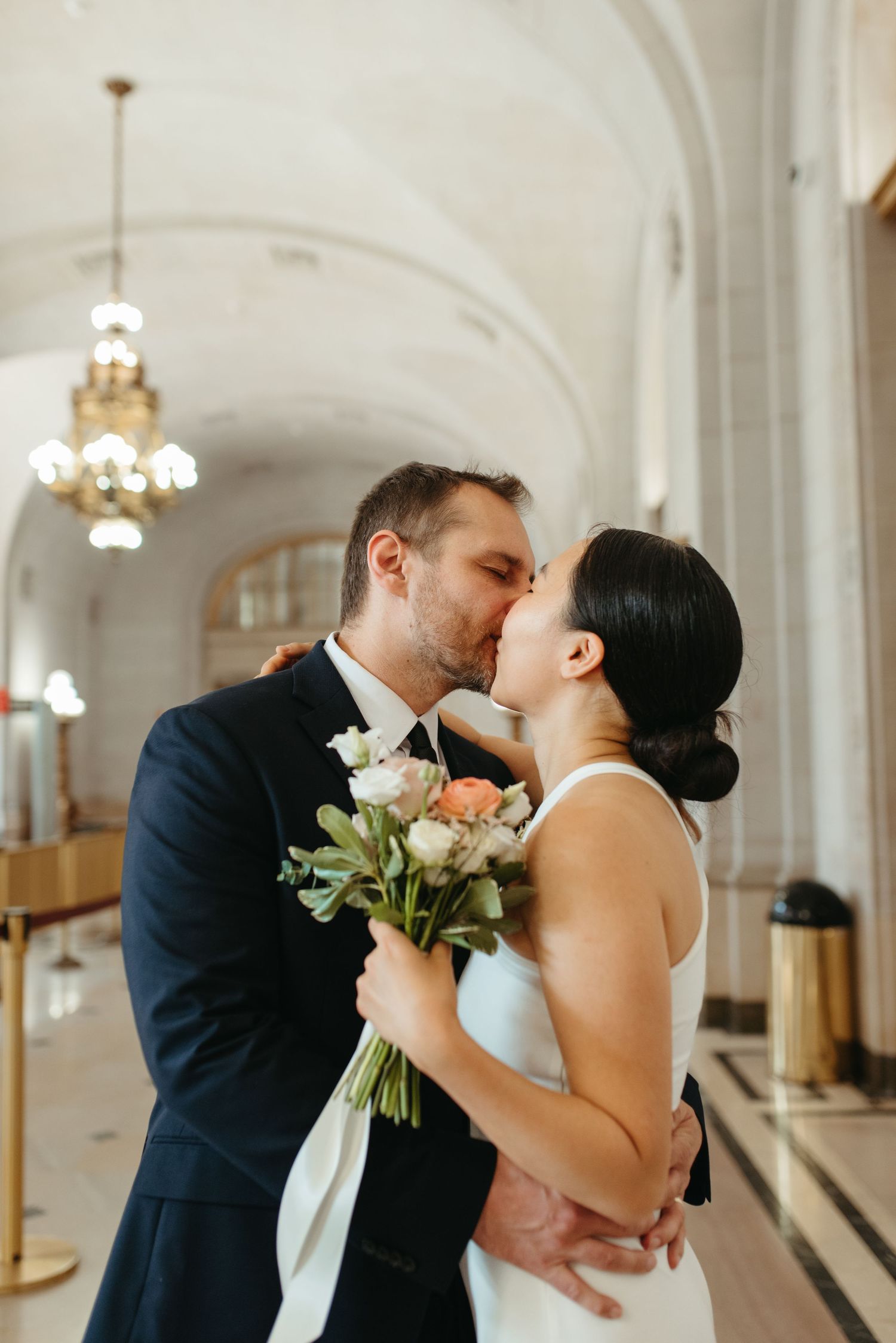 An intimate kiss between newlyweds holding a bouquet of pink and white flowers.