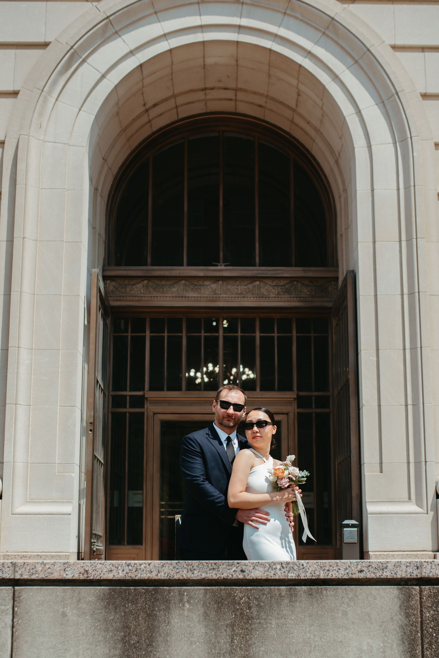 A wedding portrait of a couple standing in a grand arched doorway.