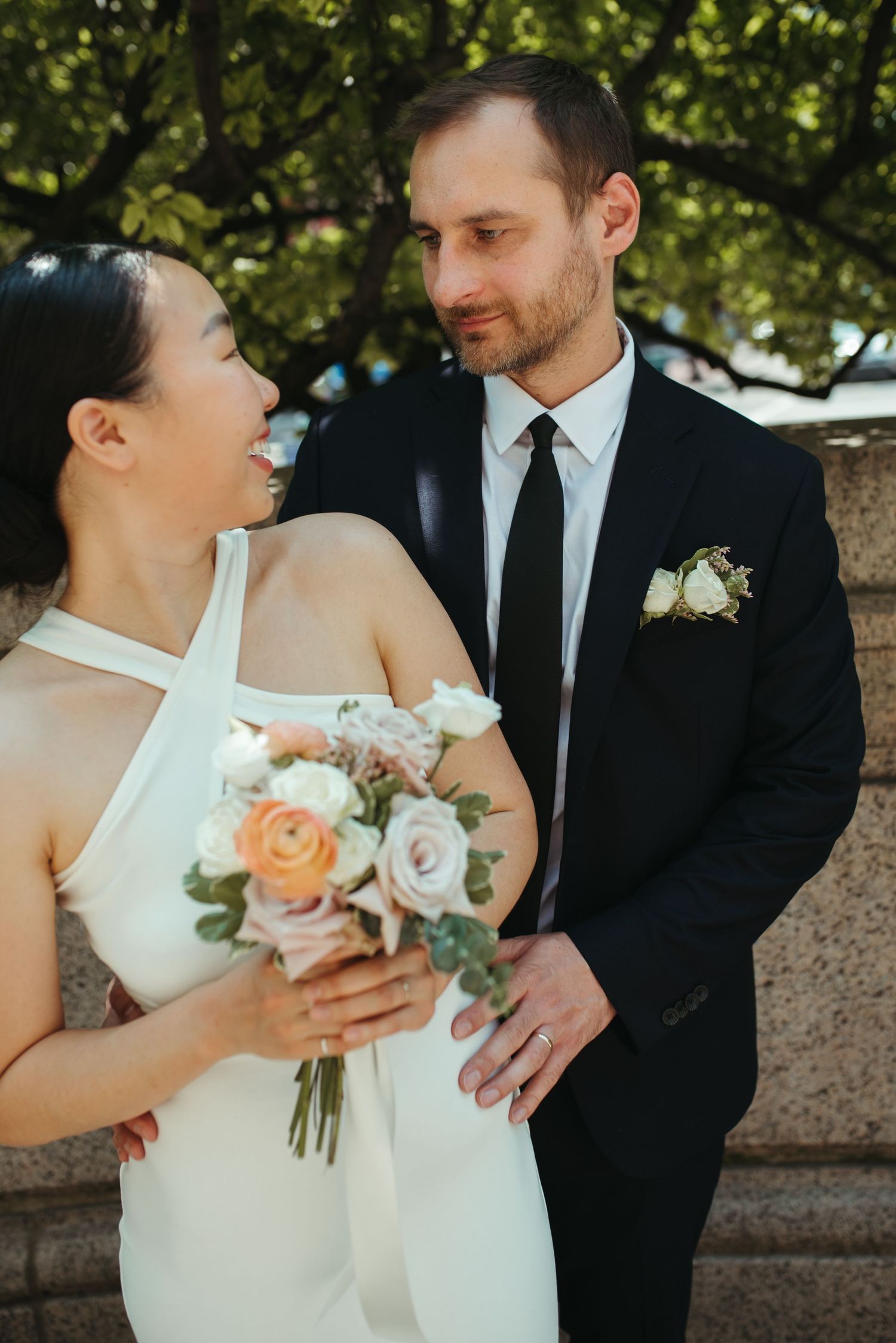 A joyful couple shares a romantic moment at their outdoor wedding ceremony with a peach and white rose bouquet.