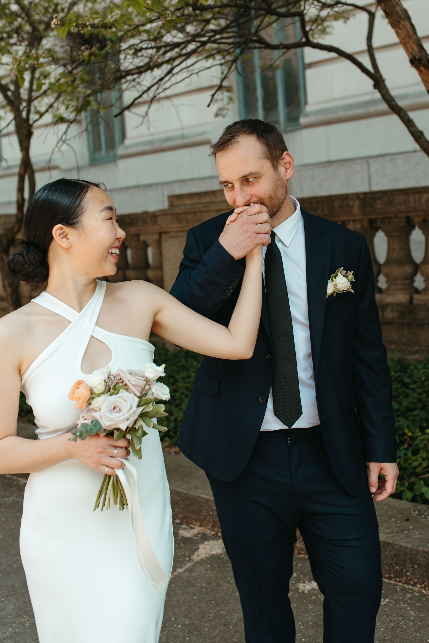 A joyful wedding couple shares a tender moment outdoors, with the bride holding a bouquet of white flowers.