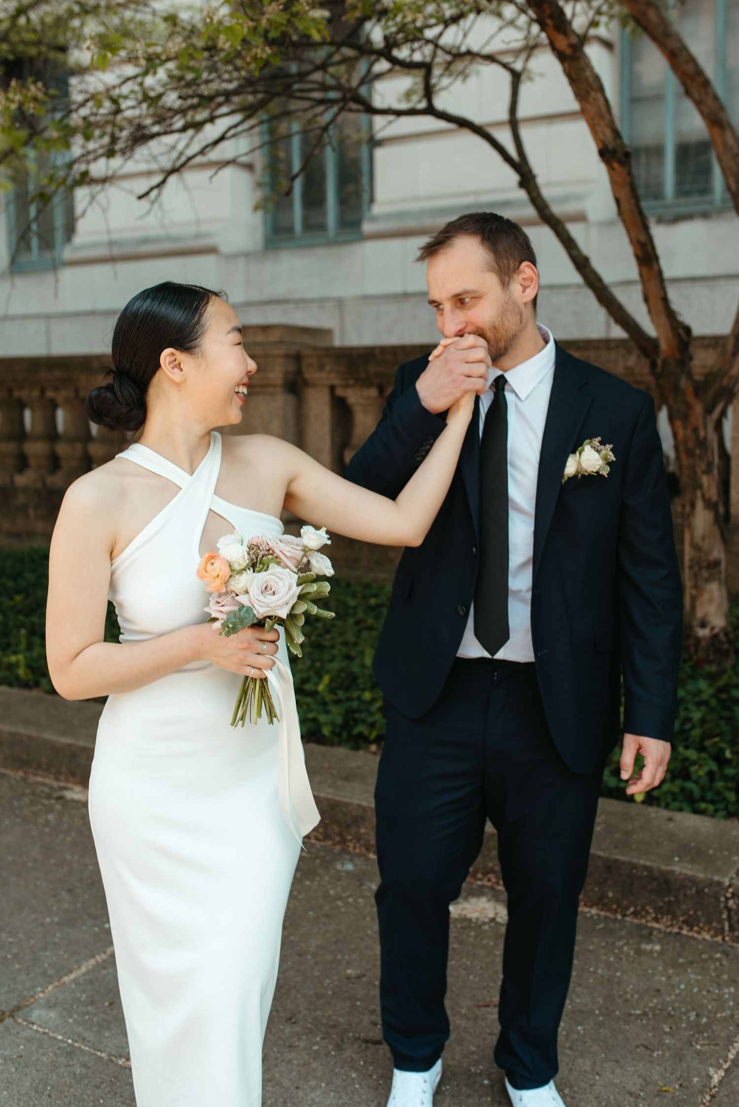A couple shares a playful moment during their wedding photoshoot in front of a historic building.