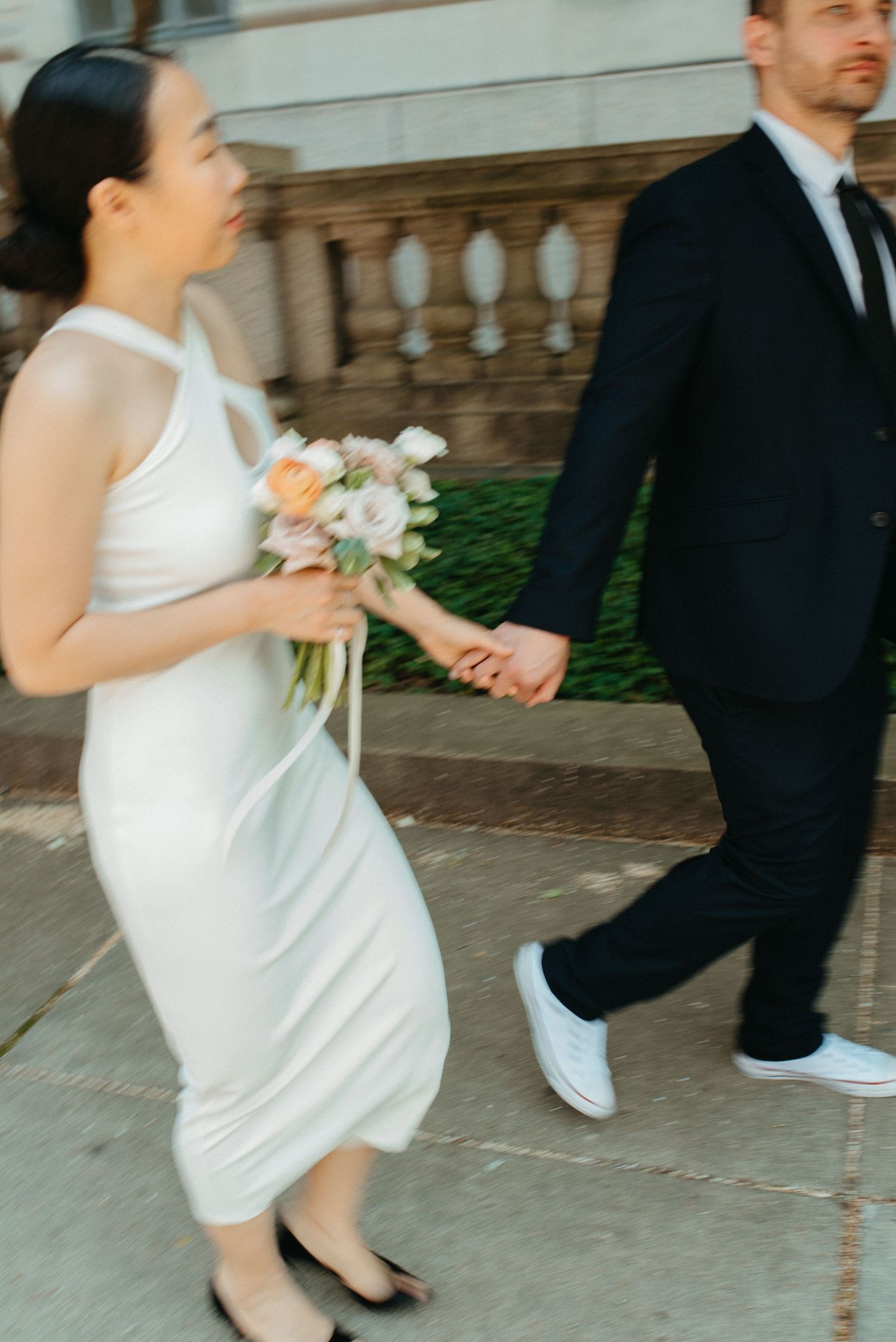 A candid moment of a bride in white dress and groom in dark suit walking together outdoors.