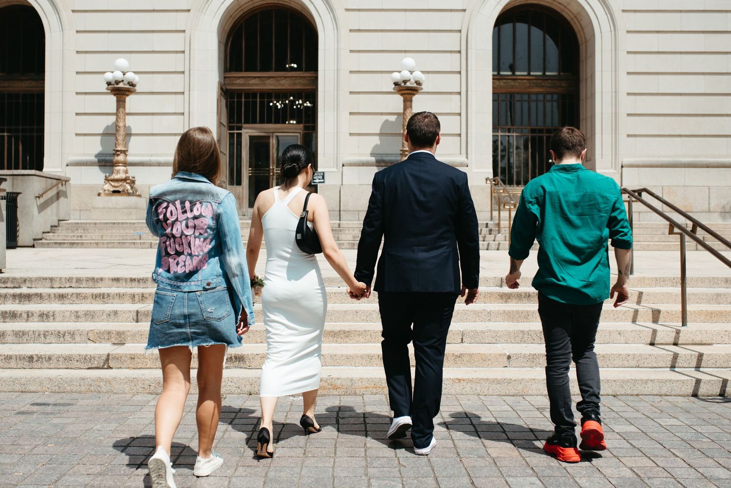 Four friends walk up elegant stone steps in front of a grand building entrance.