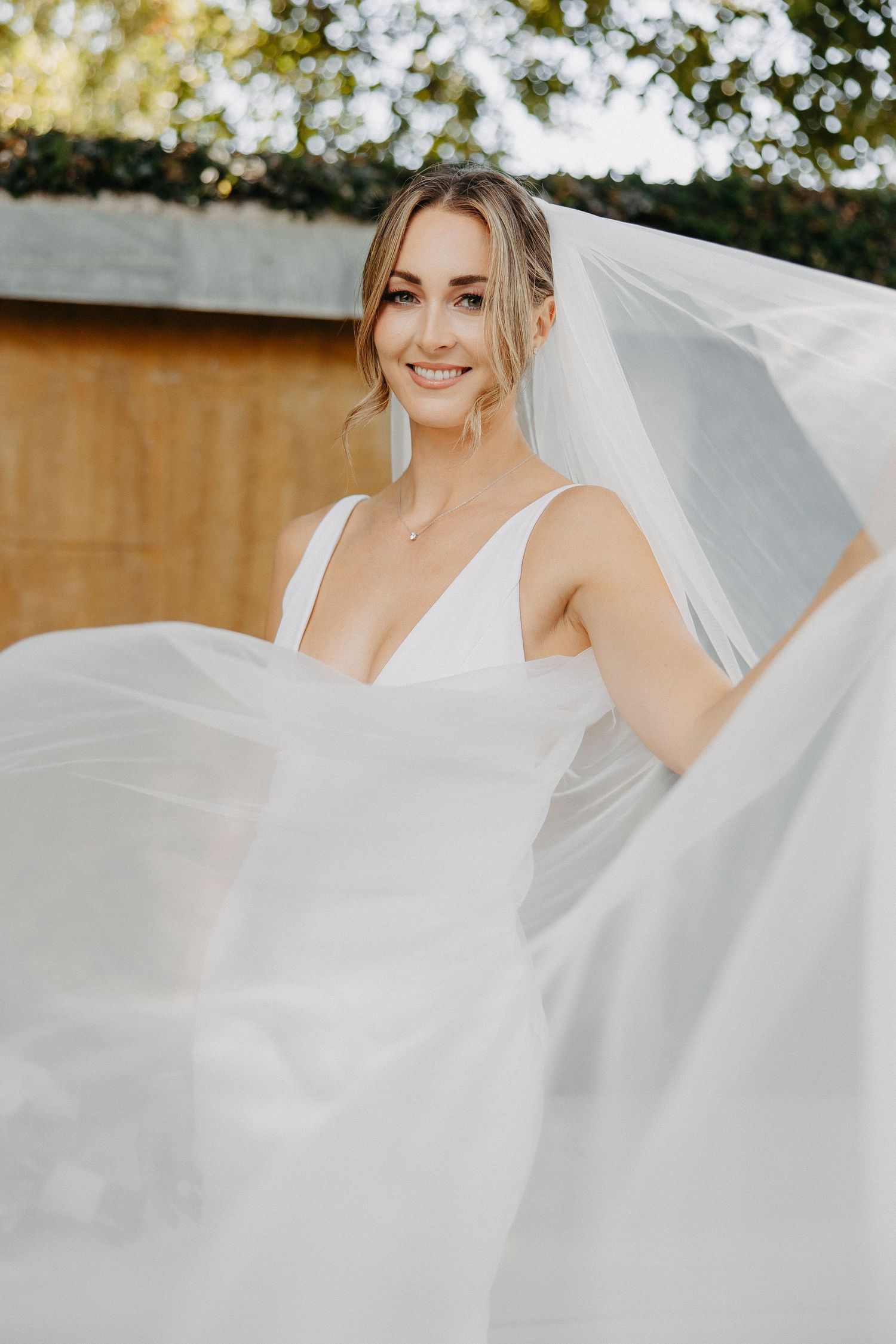 Ethereal bridal portrait with flowing veil against garden backdrop.