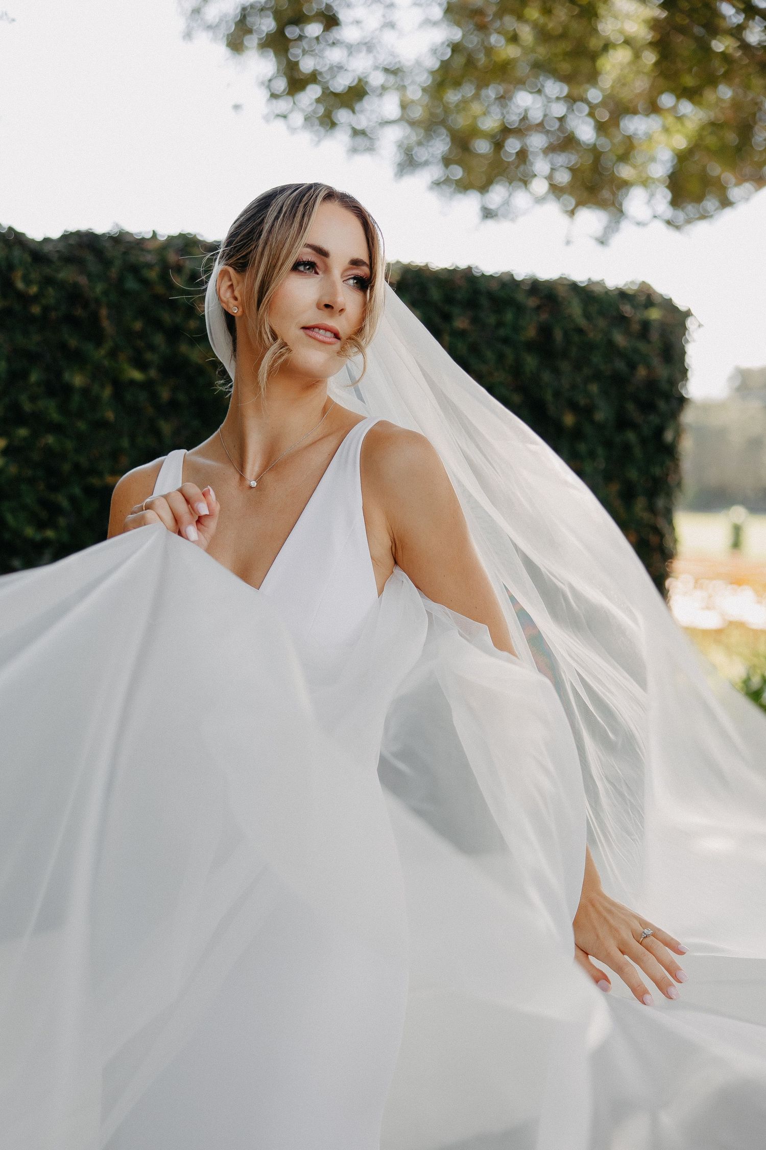Elegant bridal portrait with dramatic flowing veil against garden setting.