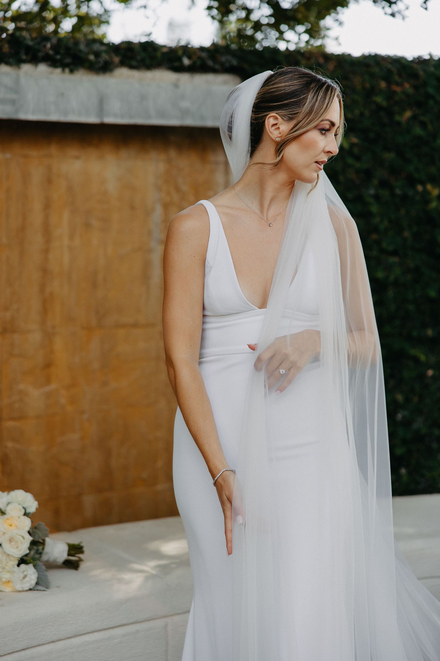 Bride wearing plunging v-neck wedding dress poses against garden backdrop with delicate veil.