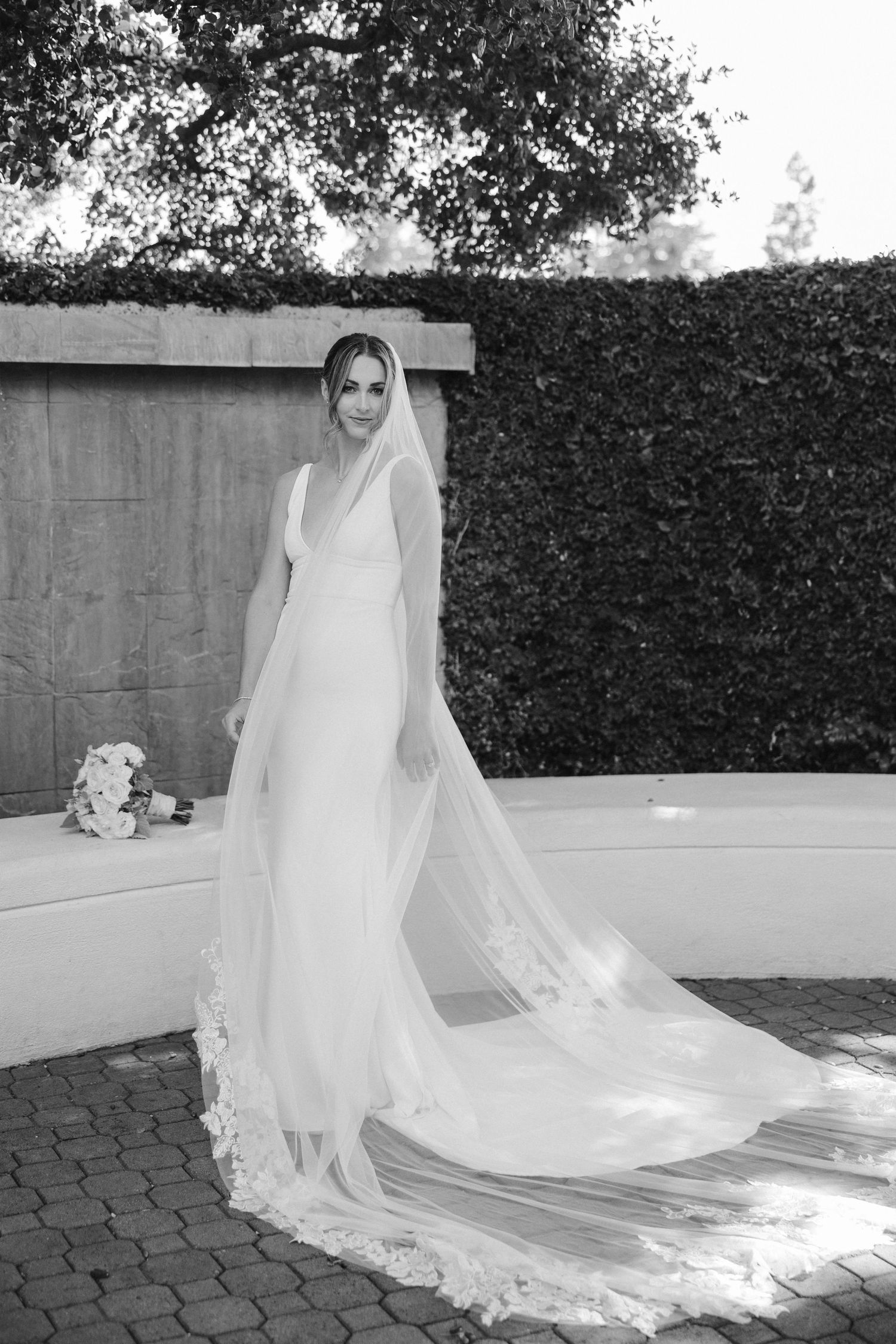 Classic black and white bridal portrait showing full-length dress and cathedral veil on brick patio.