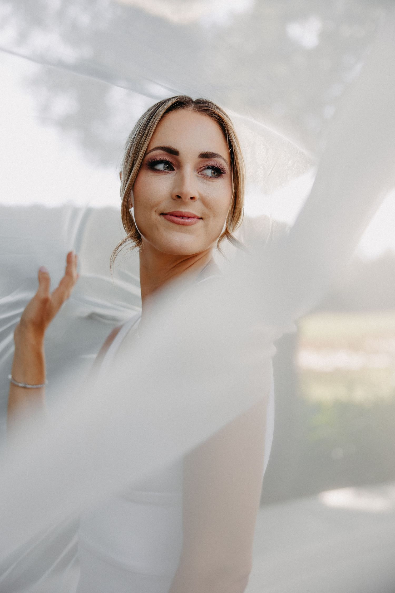 Close-up portrait of bride smiling through sheer veil outdoors.