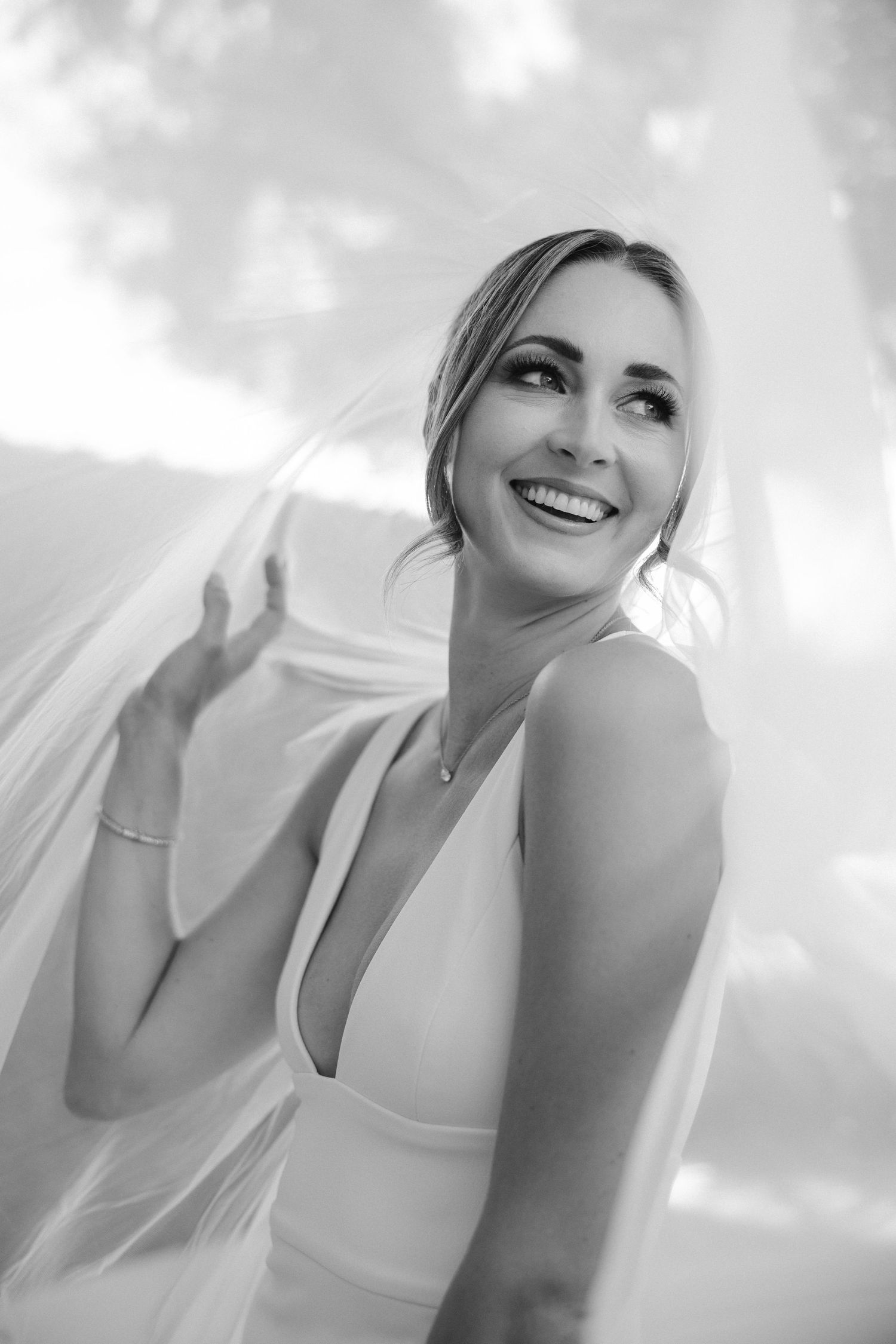 Black and white candid shot of bride laughing while playing with veil.