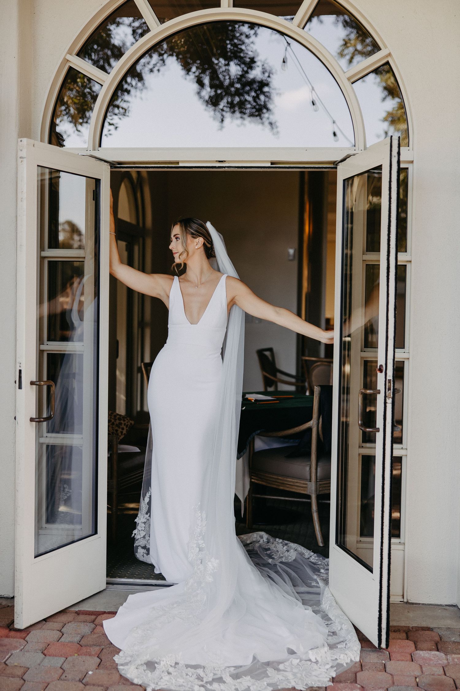 Bride in fitted wedding dress poses in arched doorway with flowing train.