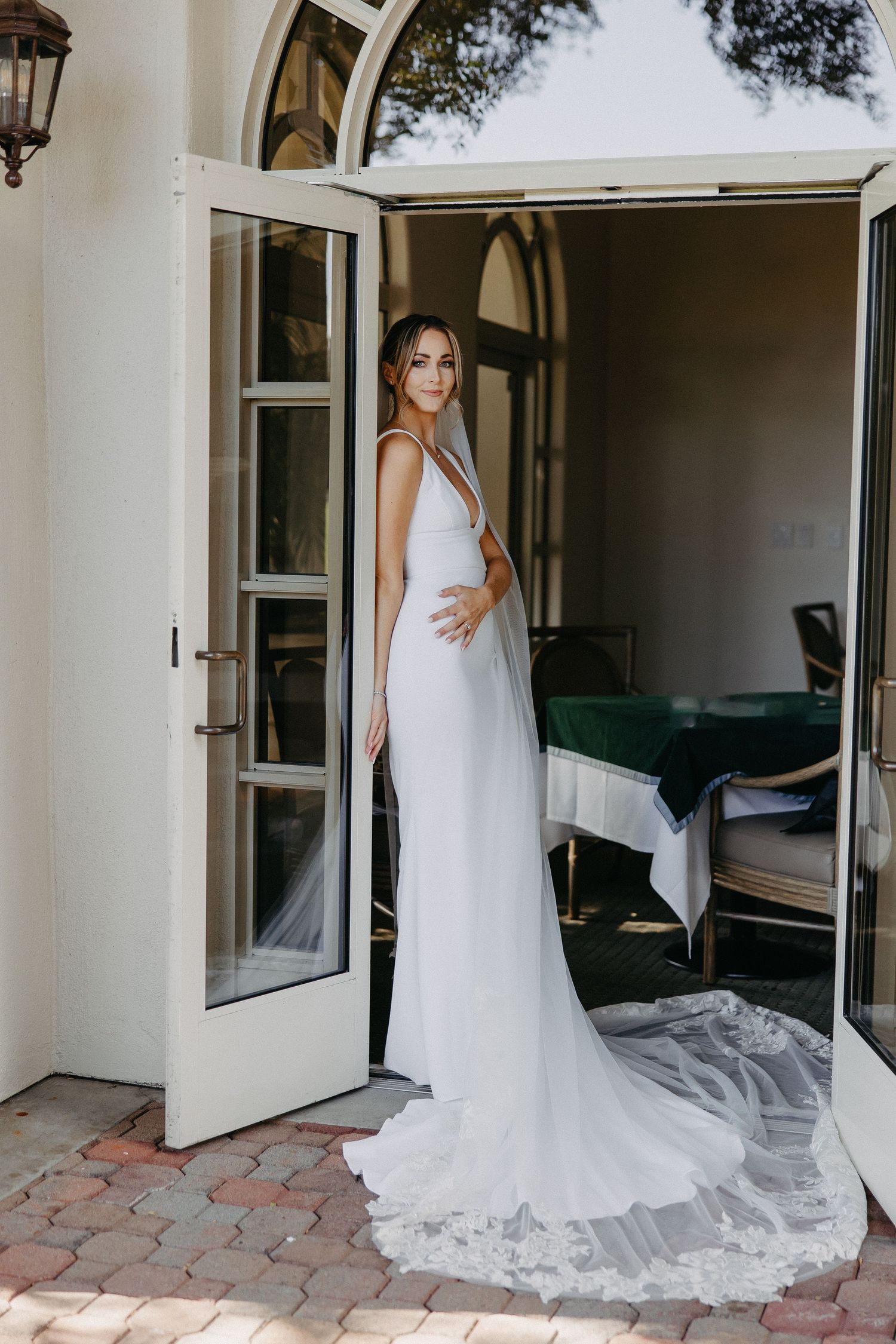 Sleek white wedding gown with dramatic train framed by French doors in elegant venue setting.